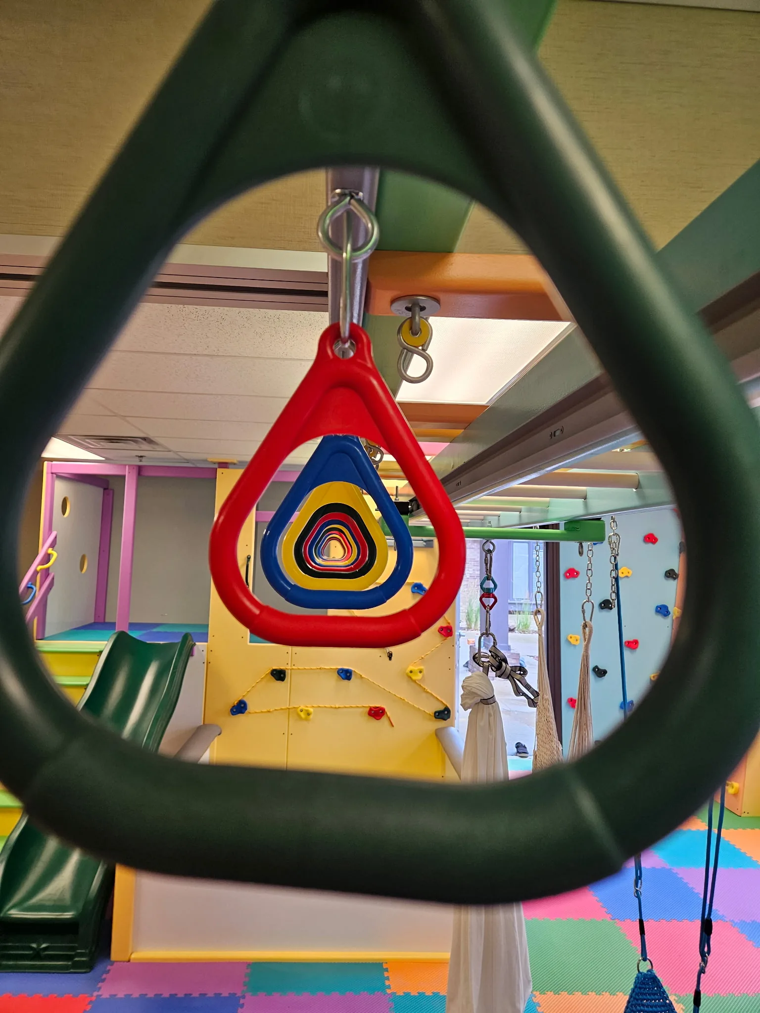 Colorful trapeze rings hanging in a row from an overhead track, seen through a green ring