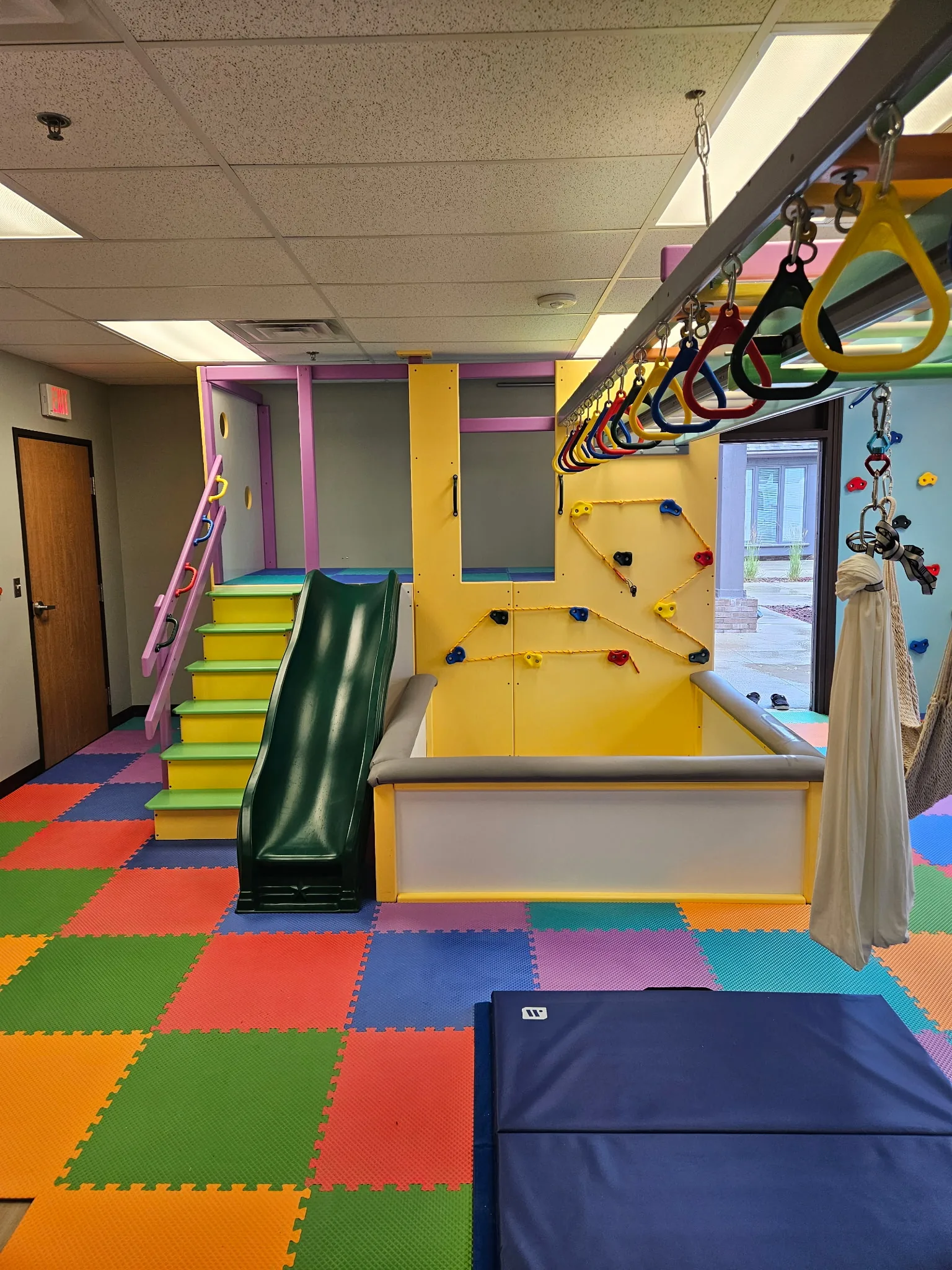Yellow climbing tower with green steps, a green slide, a ball pit, and an overhead ring track